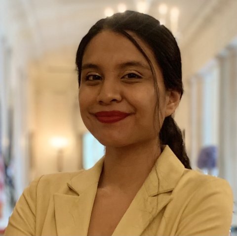 A woman smiles at the camera with a soft focus background of a political building