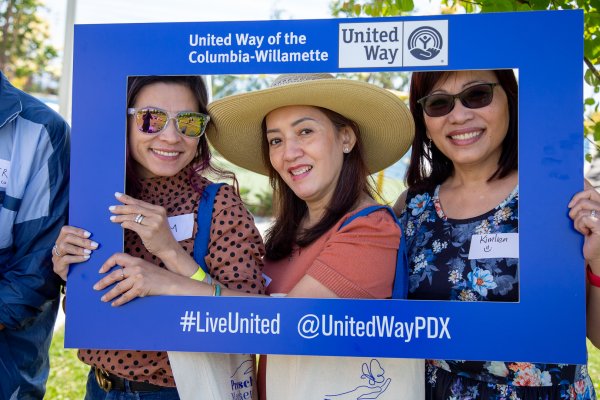 Three women pose smiling with a United Way of the Columbia-Willamette sign