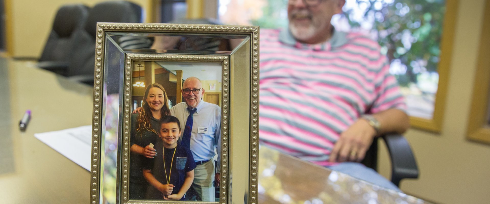 A man, blurred in the background, sits behind a photo of himself and his family