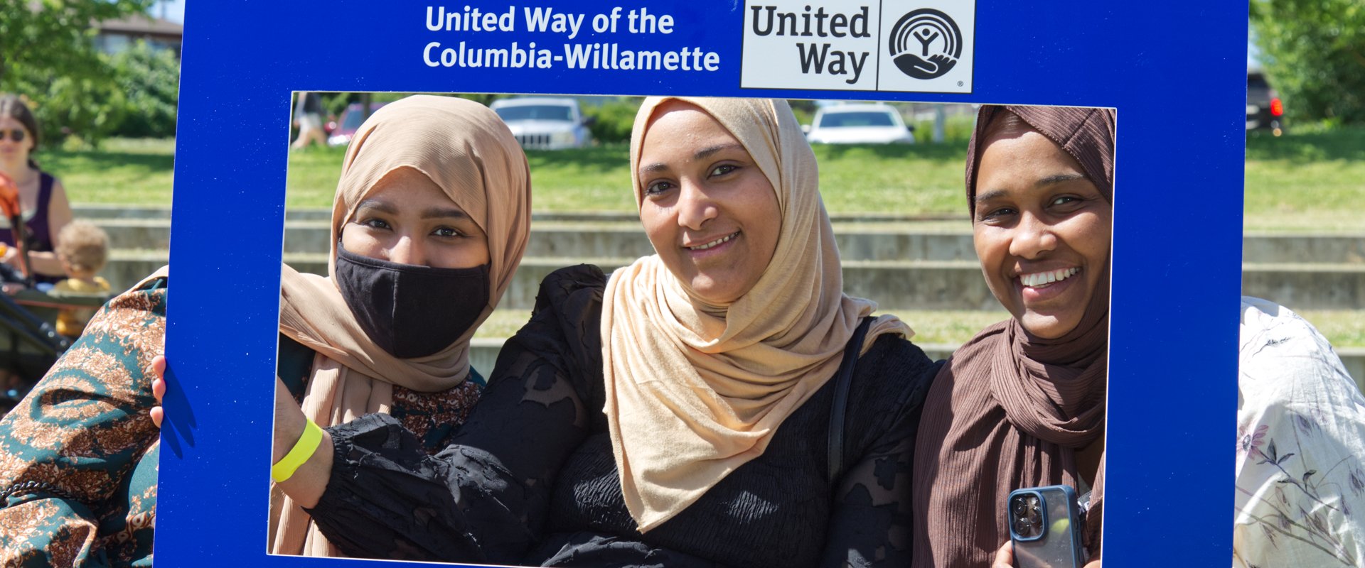 Three women pose smiling with a United Way of the Columbia-Willamette sign