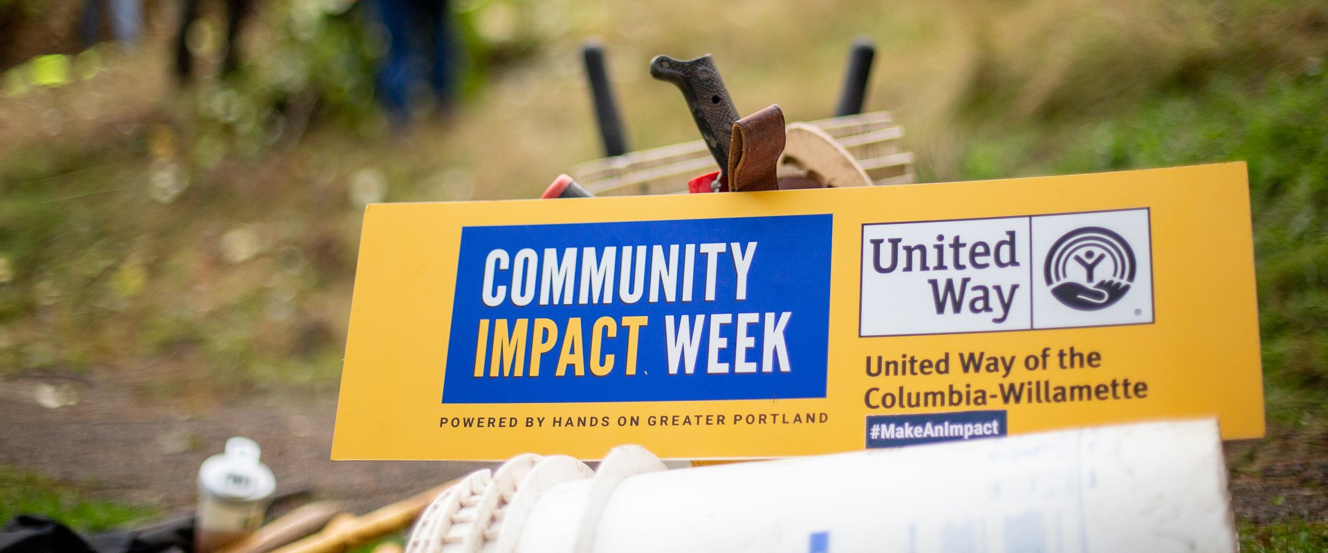 Folks work in a garden with a sign saying Community Impact Week in frame