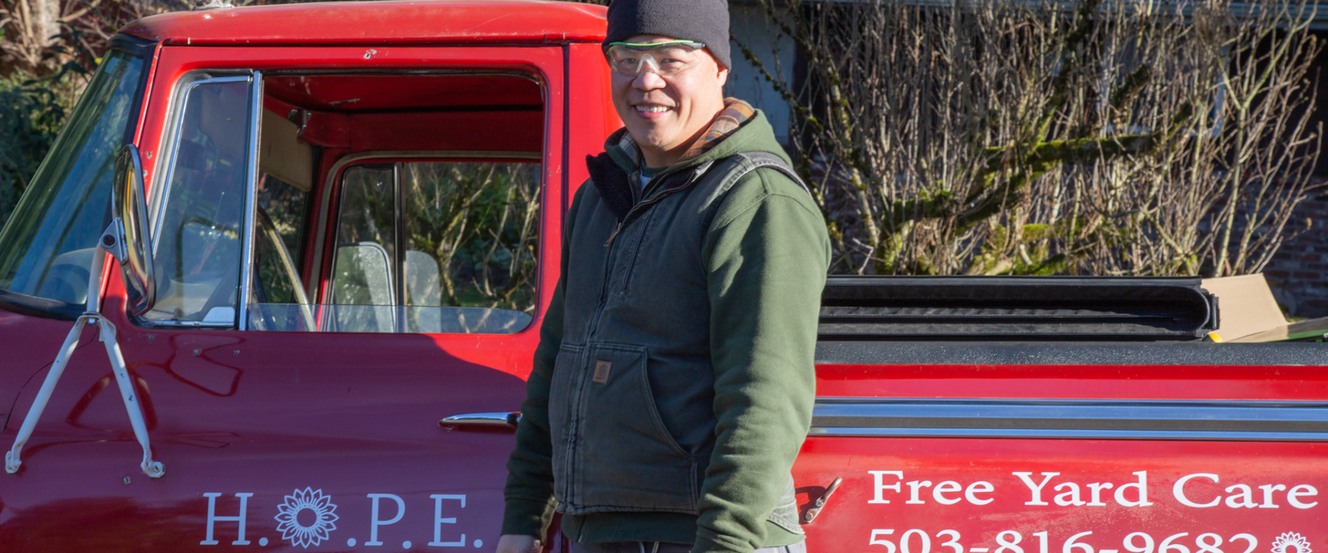 A man in a beanie stands next to a red truck