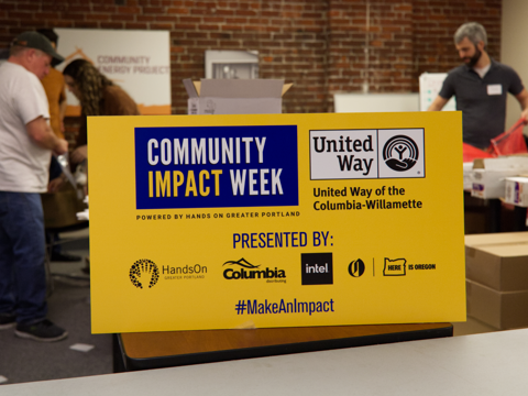 A photo of the sign for Community Impact Week with volunteers working in the background