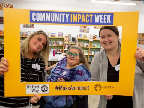 Three people hold a sign saying Community Impact Week
