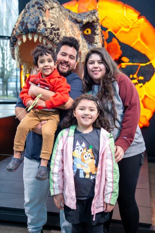 A family of five smiles in front of a LEGO T Rex