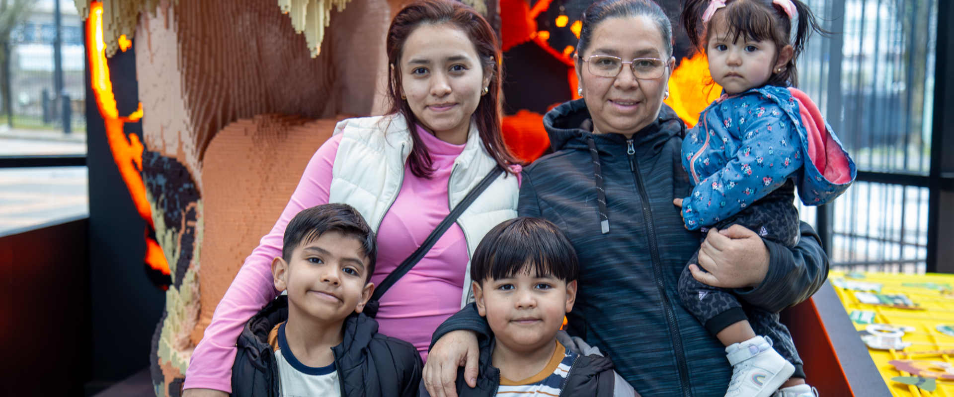 a family of five smiles in front of a lego trex